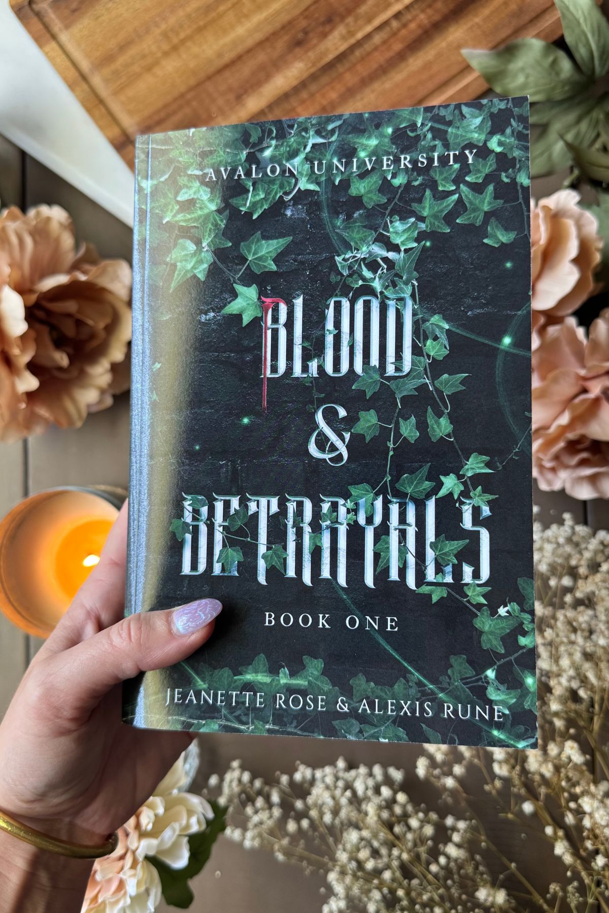 Blood & Betrayals flat lay with flowers and candle