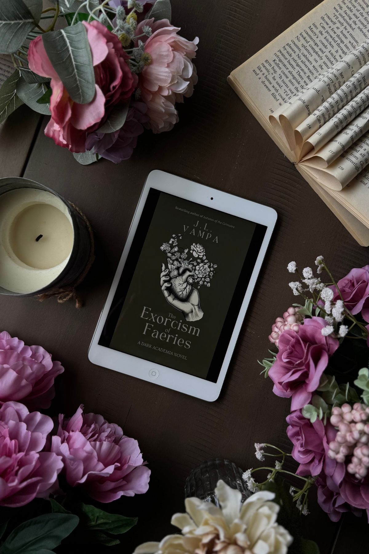 The Exorcism of Faeries book on an iPad flat lay with flowers and an open book