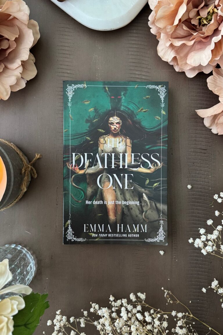 the deathless one book on an iPad flat lay with flowers and an open book